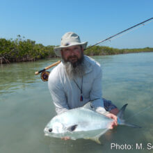 bearded man with fishing pole holding fish in water