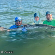 three men holding large fish in ocean