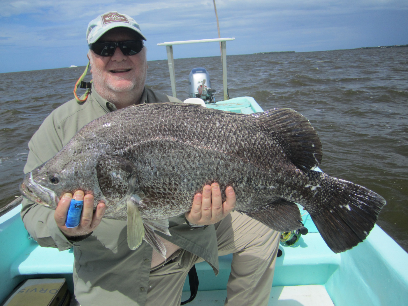 man in sunglasses holding large fish on a boat