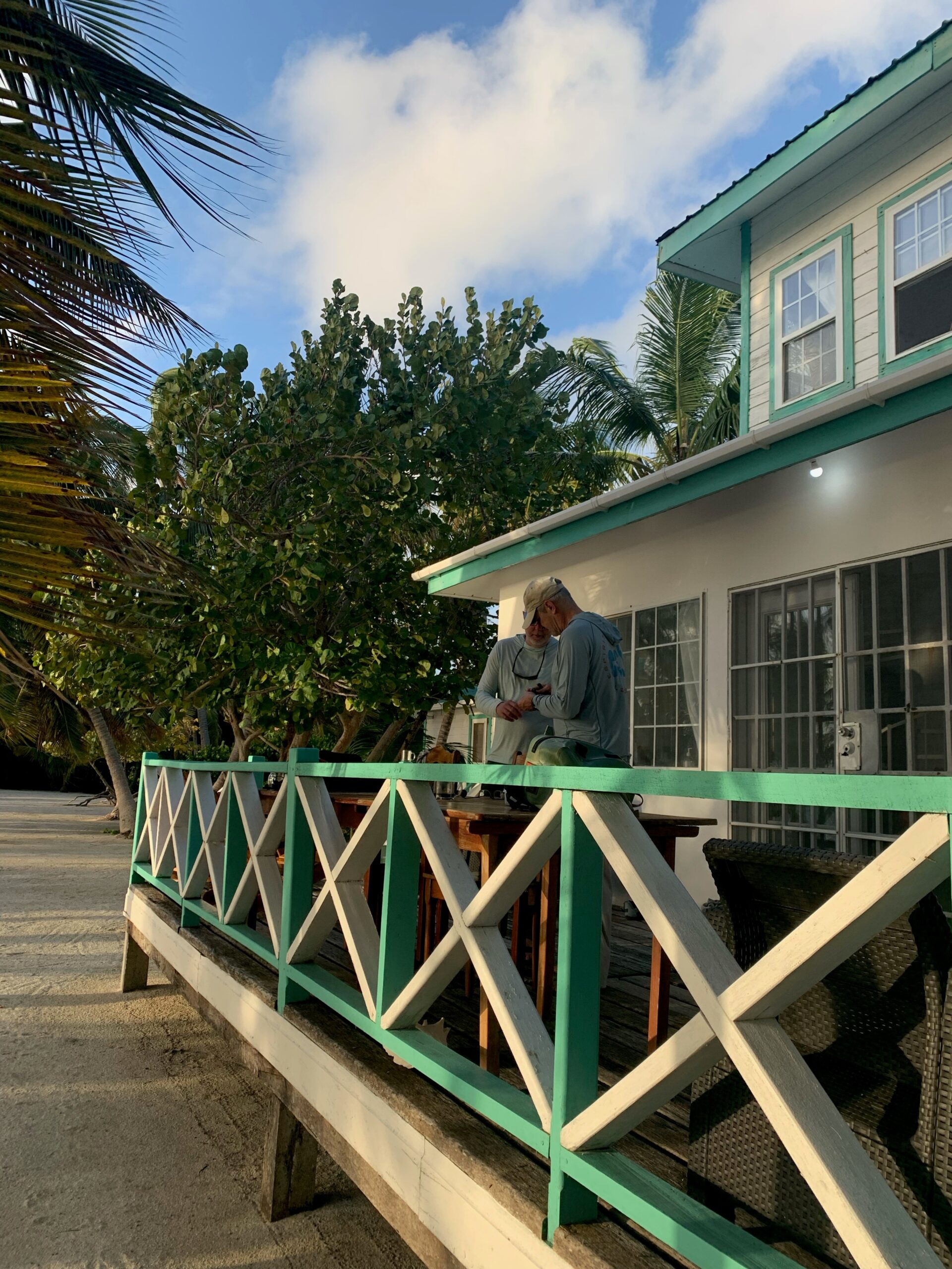 two men on balcony of a white house with teal accents